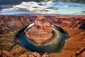 Horseshoe Bend in Page, Arizona, with dramatic clouds above the Colorado River curving around red sandstone cliffs.