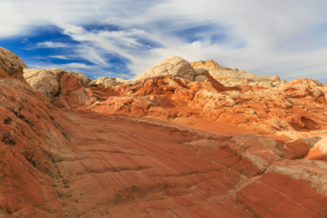 White Pocket sandstone in Vermilion Cliffs National Monument, Arizona, with smooth red rock slabs and white domes under a streaked desert sky.