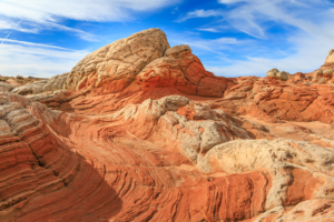 Striped sandstone formations at White Pocket in Vermilion Cliffs National Monument, Arizona, with vivid red and cream rock layers under a blue sky.