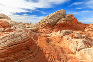 Layered sandstone formations in White Pocket with red and white striations under a bright blue sky.
