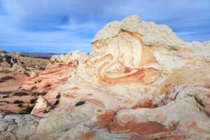 Swirling red, orange, and white sandstone formations at White Pocket under a soft blue sky.