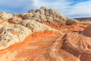 White Pocket sandstone domes with cream-colored rock over red desert layers under a bright sky.