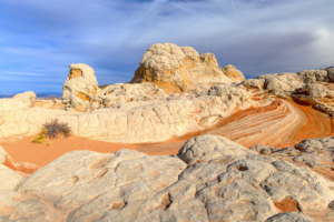 White Pocket sandstone formations with cream-colored domes and red striated ridges under a partly cloudy sky.