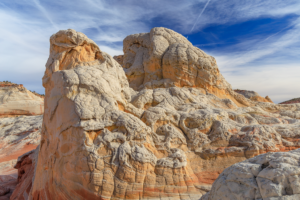 Towering White Pocket sandstone cliffs with intricate textures and warm red, orange, and cream tones under a vivid sky.