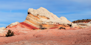Colorful sandstone formations at White Pocket in Vermilion Cliffs National Monument, Arizona, with swirling red, orange, and white rock layers under a blue sky.