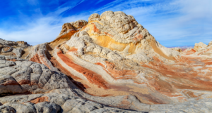 White Pocket rock formations in Vermilion Cliffs National Monument with swirling red, orange, and white sandstone under a vivid blue sky.
