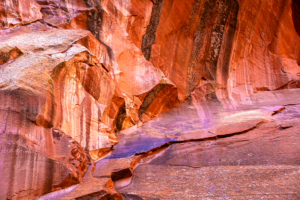 Colorful sandstone wall in Capitol Reef National Park, Utah, with streaks of red, orange, and purple tones shaped by water and erosion.