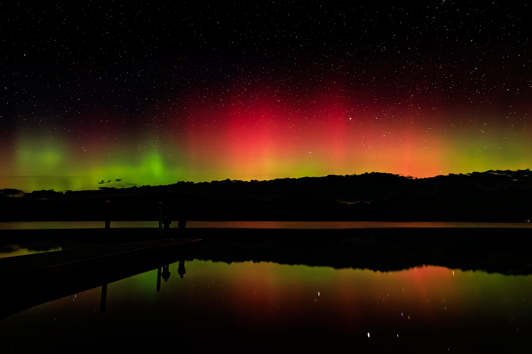 Northern Lights glowing red and green over Lake McDonald in Glacier National Park, Montana, with reflections on the water.