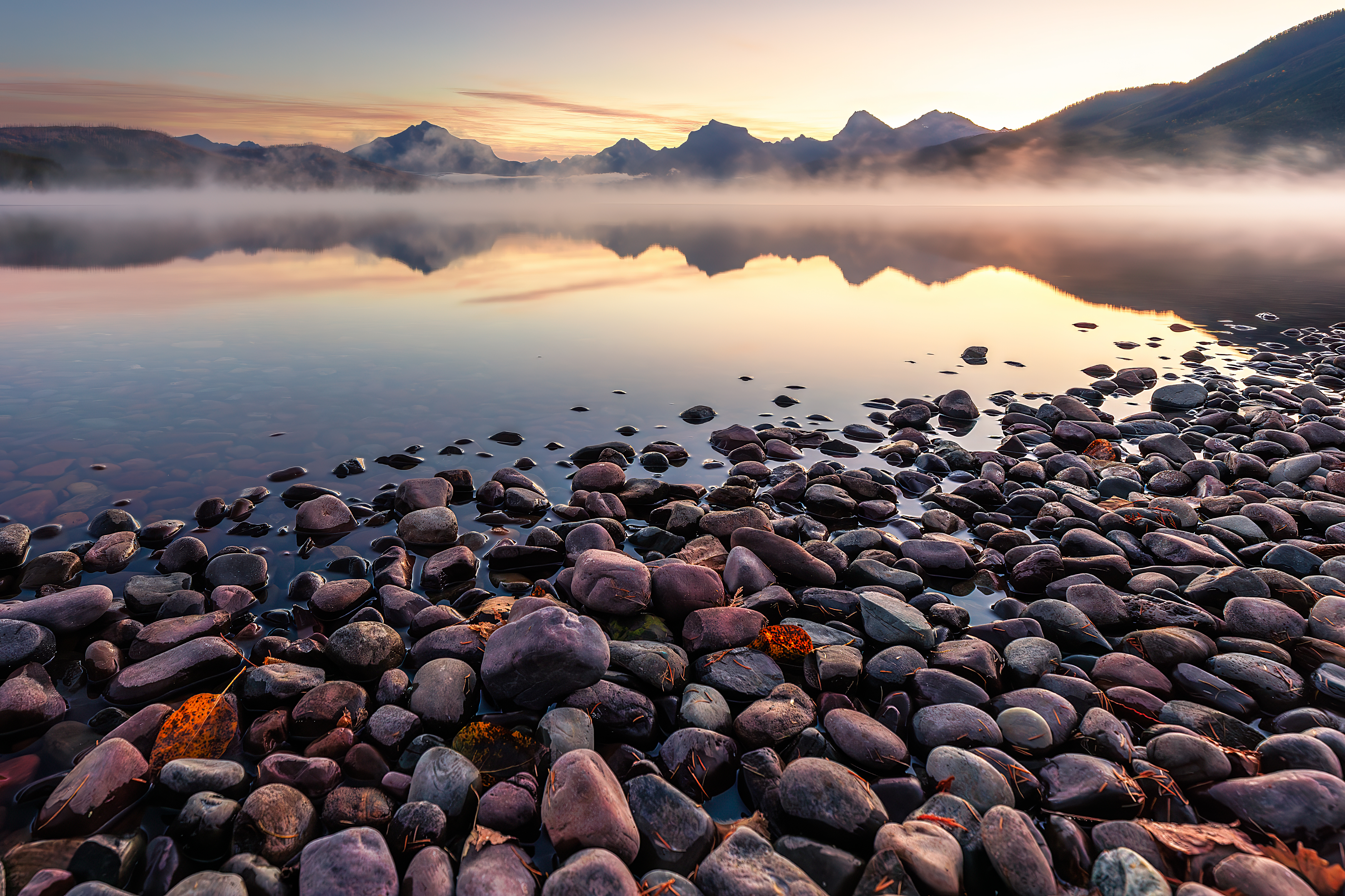 Colorful stones along the shoreline of Lake McDonald at sunrise with mountain reflections, Glacier National Park landscape photography