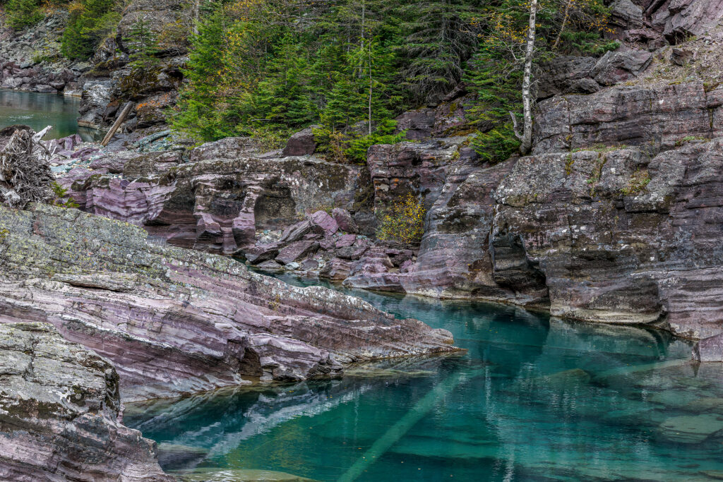 Clear turquoise water flowing through purple rock canyon, Glacier National Park landscape photography
