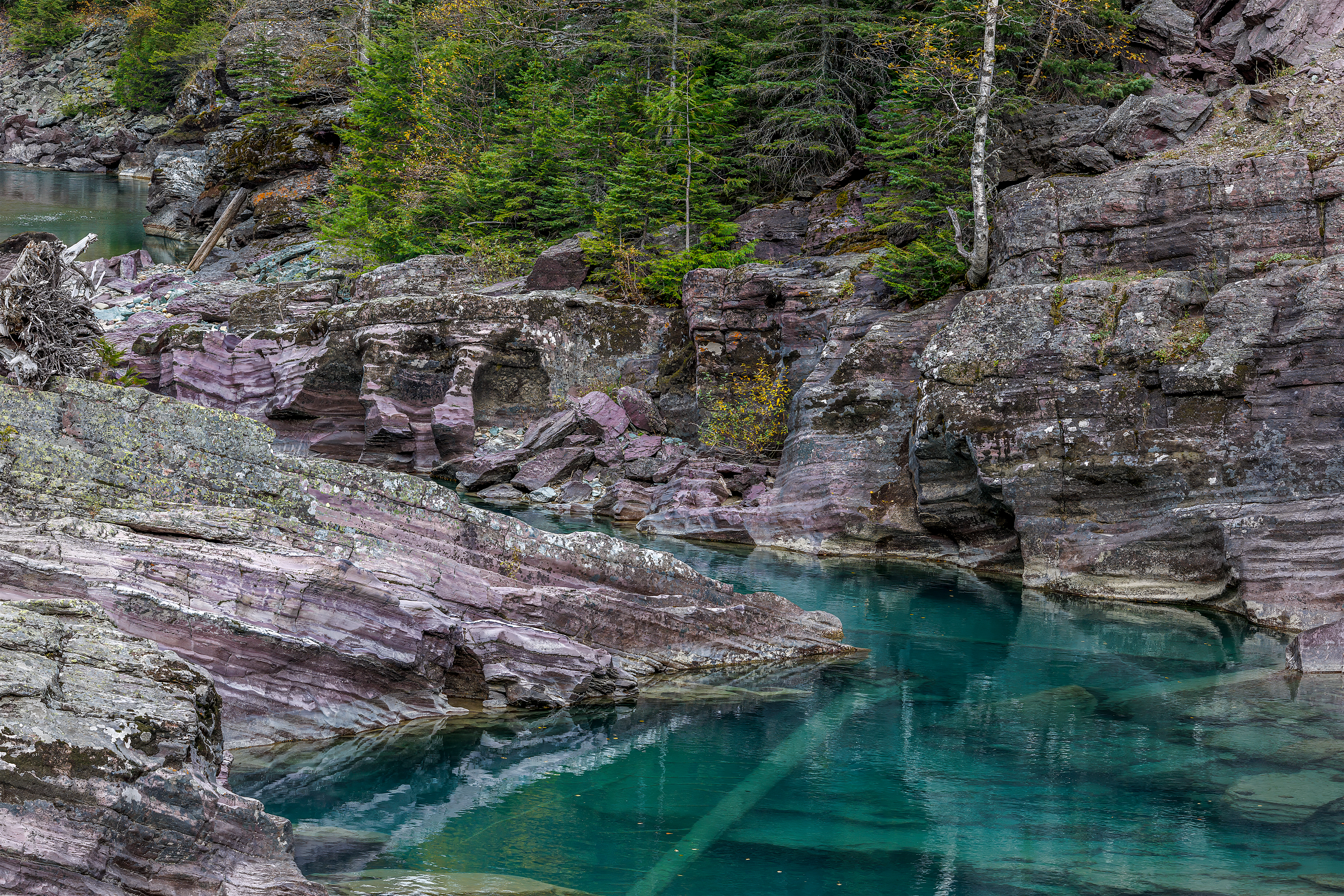Clear turquoise water flowing through purple rock canyon, Glacier National Park landscape photography