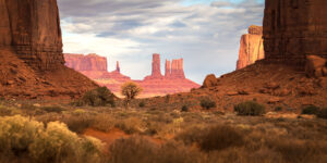 Sunlit sandstone buttes and mesas at Monument Valley framed by desert vegetation, Arizona-Utah border landscape photography
