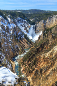 Lower Falls of the Yellowstone River in the Grand Canyon of the Yellowstone, surrounded by snowy cliffs and pine forest, Yellowstone National Park landscape photography