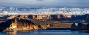 Snow capped cliffs above Lake Powell with winter light on sandstone and water